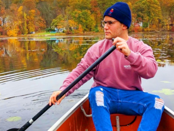 A man in a pink sweater paddles a canoe across a calm pond.